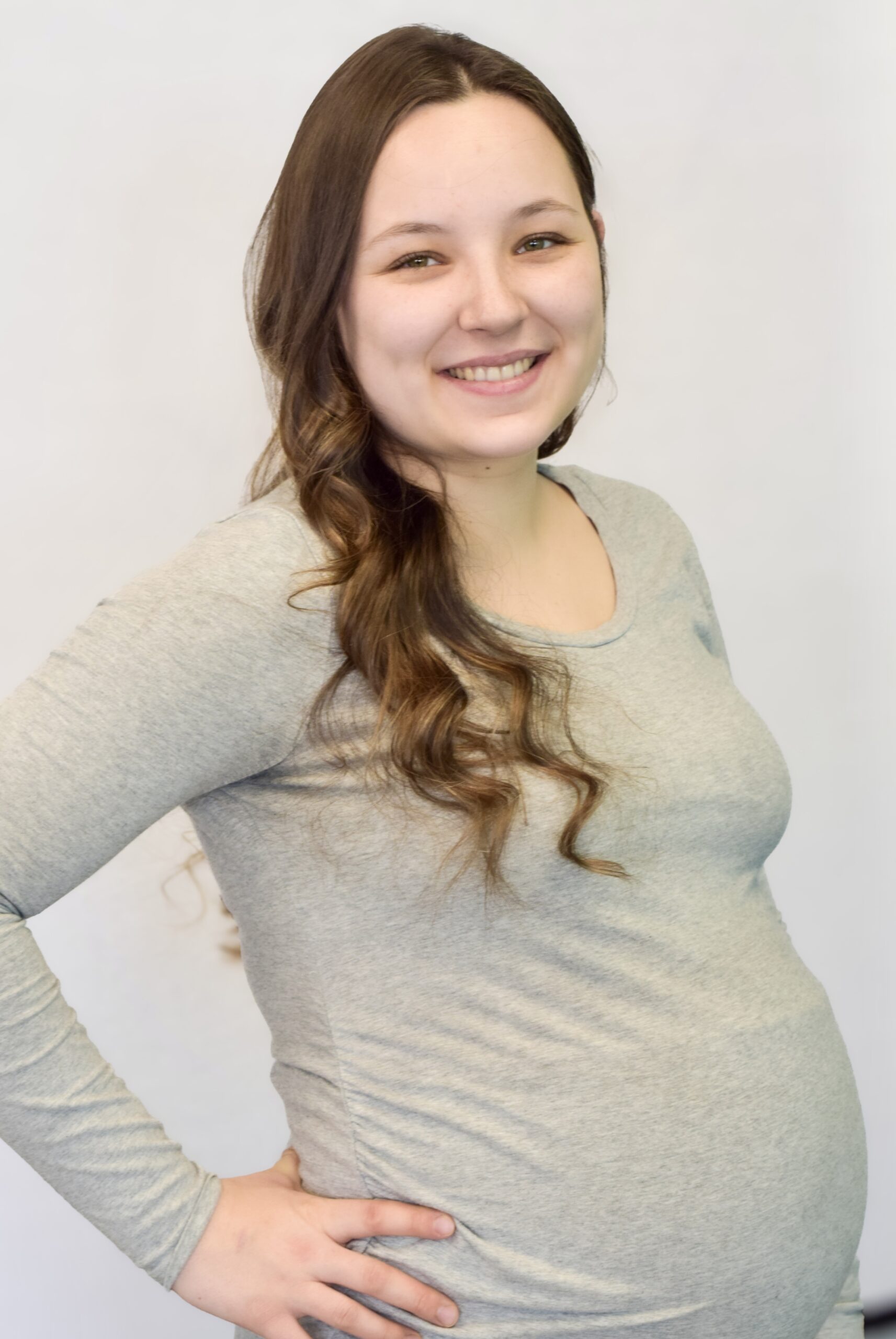 Femme enceinte aux cheveux bruns frisés avec chandail gris